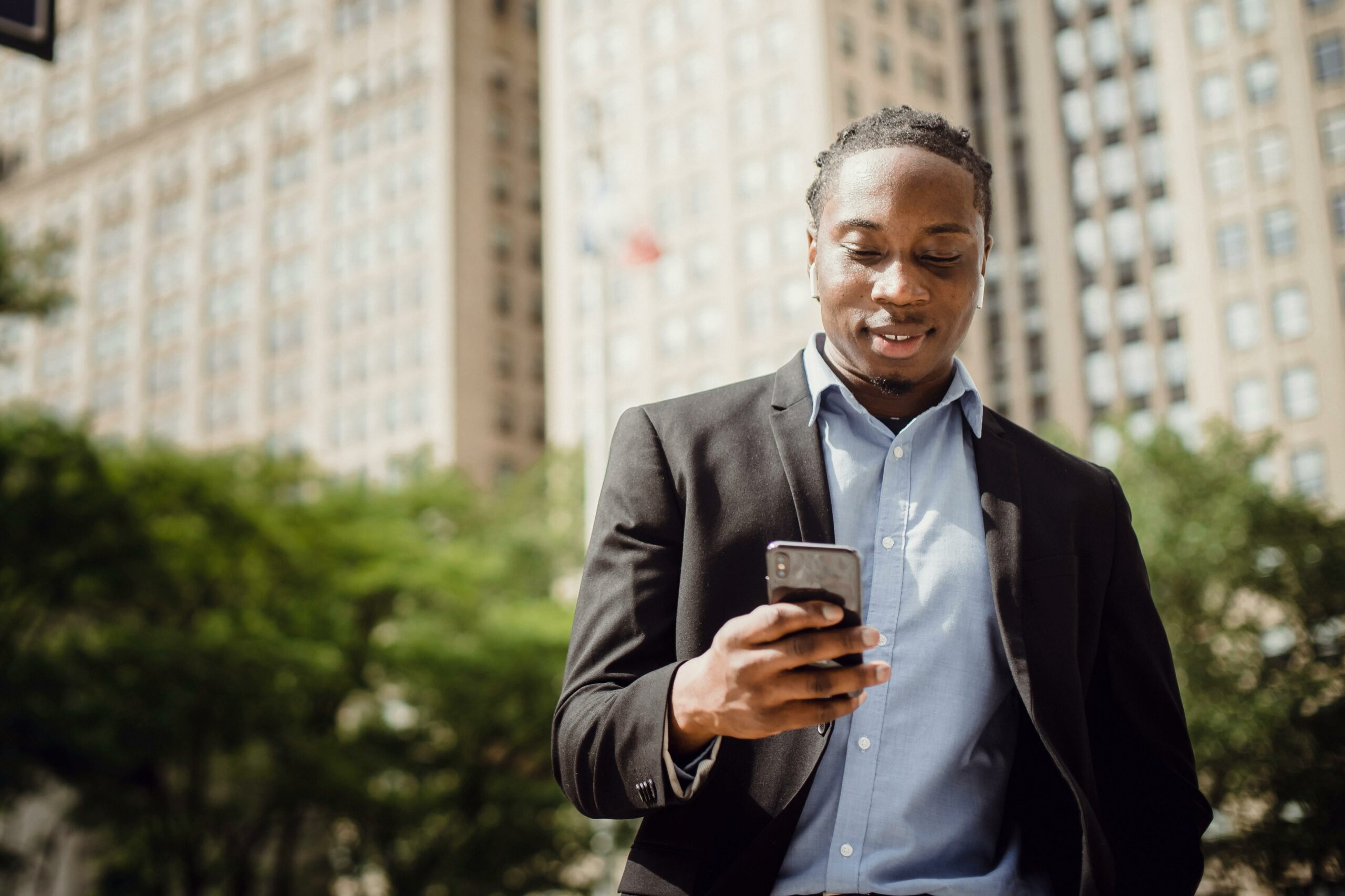 a man slightly smiling scrolling through the phone walking down the streets of a big city